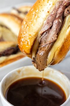 a roast beef sandwich being dunked into a cup of coffee with chocolate sauce on the side