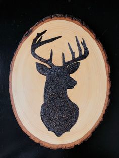 a deer head carved into a wood slice on a black background with the word,