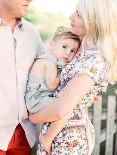 a woman holding a baby in her arms while standing next to a man with blonde hair