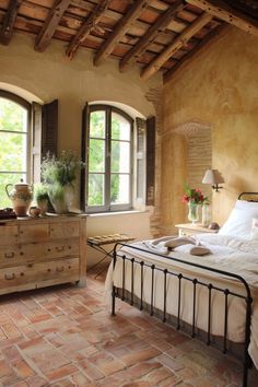 a bed sitting in a bedroom next to two windows and a dresser with vases on top of it