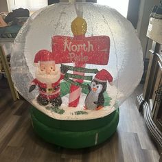 an inflatable snow globe with santa claus and penguins on it, sitting next to a sign that says north pole