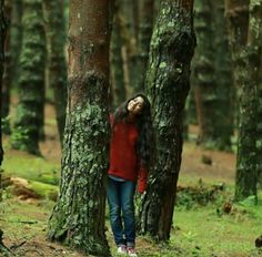 a woman standing in the middle of a forest with her head between two large trees