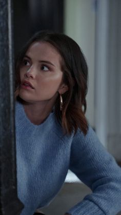 a woman in a blue sweater leaning against a wall