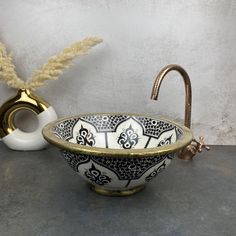 an ornate bowl with gold rim sits on a counter next to a vase and faucet