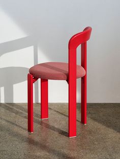 a red chair sitting on top of a floor next to a white wall with a shadow cast on it