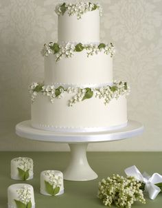 a three tiered cake with white flowers and leaves on the top is surrounded by small cubes