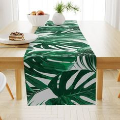 a table with a green and white tropical print runner on it, next to a bowl of fruit