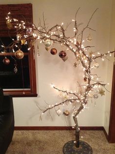 a christmas tree with ornaments and lights on it in front of a window, next to a couch