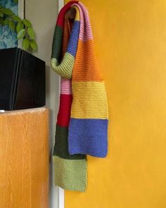 a multicolored towel hanging on a yellow wall next to a wooden shelf with a potted plant