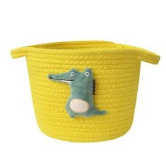 a yellow basket with a stuffed alligator on the side and a green toy in the middle