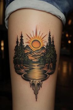 a woman's thigh with an image of mountains and trees on it, while the sun is setting