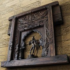 an ornate wooden frame with a statue on it's side against a brick wall