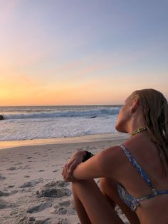 a woman sitting on top of a sandy beach next to the ocean