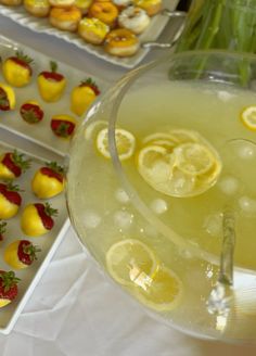 a pitcher filled with lemonade next to trays of donuts and strawberries