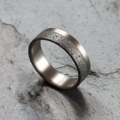 a wedding band with silver flecking on it sitting on top of a stone slab