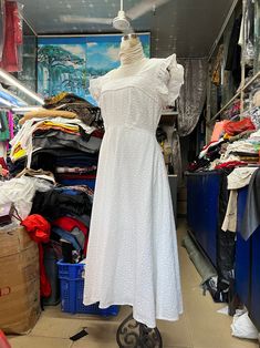 a white dress sitting on top of a metal object in a room filled with clothes