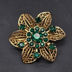 This vintage rhinestone flower brooch features a gold tone filigree flower with green rhinestones and measures 1.25" D Green Flower Shaped Brooch Pins, Green Flower Brooch Pins, Green Flower-shaped Brooch Pins, Elegant Green Filigree Brooches, Green Flower-shaped Brooches For Weddings, Antique Green Filigree Brooches, Green Filigree Brooches For Gifts, Green Filigree Brooches As A Gift, Green Filigree Brooches As Gift