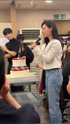 a woman standing in front of a cake while holding a microphone to sing into it