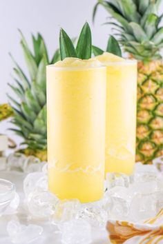 two glasses filled with yellow liquid next to pineapples