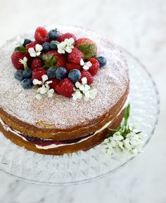 a cake covered in powdered sugar with berries and blueberries on top is sitting on a glass plate