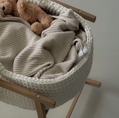 a brown teddy bear laying in a basket on top of a wooden chair next to a white wall