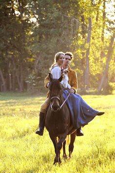 a man and woman riding on the back of a brown horse through a lush green field