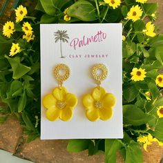 a pair of yellow flower shaped earrings sitting on top of a card next to flowers