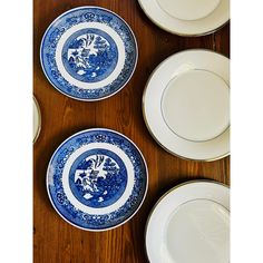 four plates with blue and white designs on them sitting on a wooden table next to silverware