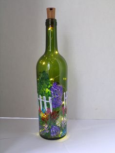 a green glass bottle with flowers painted on the side and lights in the top, sitting on a white surface