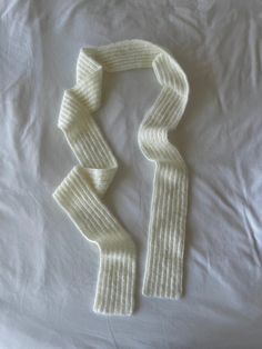 two white knitted scarfs laying on top of a bed next to each other