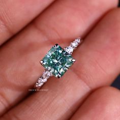 a close up of a person's hand holding a ring with a green diamond