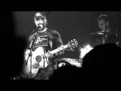 the man is playing his guitar on stage with other people in the audience behind him