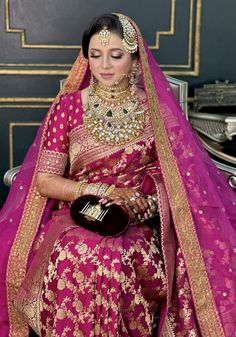 a woman in a pink and gold bridal outfit sitting on a chair with her hands clasped to her chest