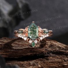 an emerald and diamond ring sitting on top of a tree stump in front of some rocks