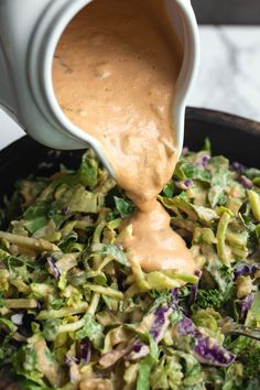 someone pouring dressing onto a salad in a skillet with broccoli and purple cabbage