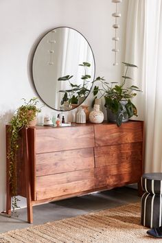 a wooden dresser topped with plants next to a round mirror on top of a wall