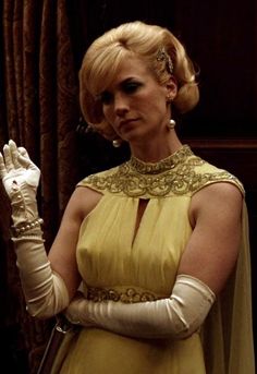 a woman in a yellow dress is holding her hand up to the side while wearing white gloves