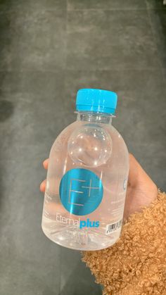 a person holding a plastic water bottle with a blue cap on it's top