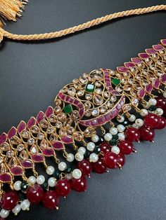 the necklace is adorned with red and white stones, pearls, and tassels