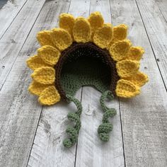 a crocheted sunflower hat is laying on the wooden floor with it's tail curled up