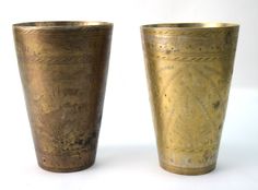 two old brass cups sitting side by side on a white surface with no one around them