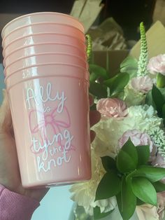 a person holding a pink cup with flowers in the background