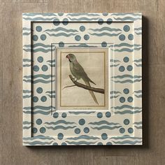 a bird sitting on top of a wooden table next to a framed print with blue and white circles