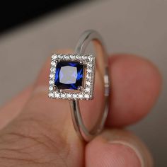 a hand holding a ring with a blue stone in it's center and diamonds around the band