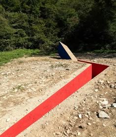 there is a red and blue object in the middle of a dirt field with trees behind it