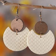 two white and brown circular earrings hanging from a tree branch with leaves in the background