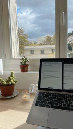 an open laptop computer sitting on top of a wooden desk next to a plant and potted cacti