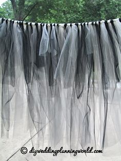 black tulle curtain hanging on the side of a building with trees in the background