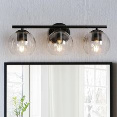 a bathroom vanity with three lights and a mirror on the wall next to a potted plant