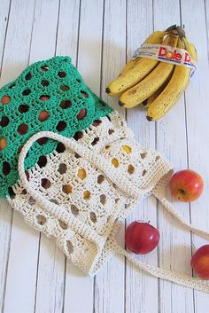 two crocheted purses with apples and bananas next to them on a white wooden surface